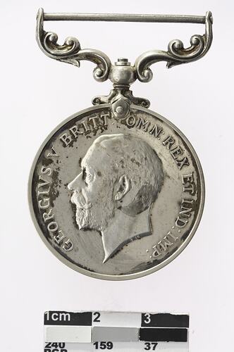 Silver coloured medal with profile of a man and text surrounding.