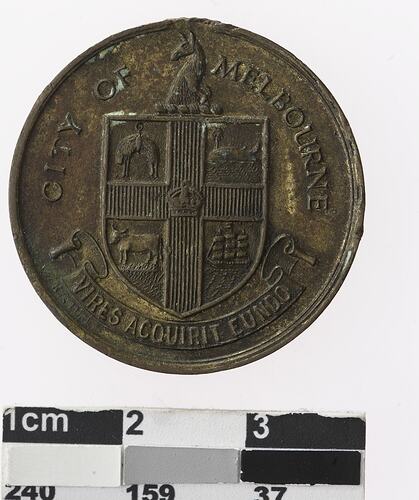 Round rusted medal with coat of arms, text surrounding.