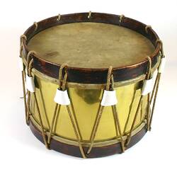 Cylindrical shiny brass drum, wooden edges, natural skin. Rope threaded around drum.