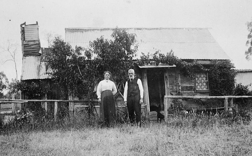 An elderly man and a woman in front of a small weatherboard house.