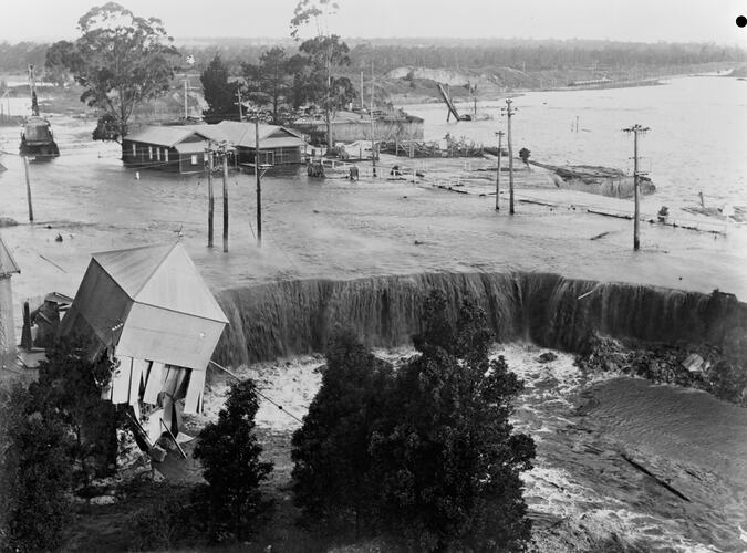 [A building teeters on the edge of the coal mine as flood waters surge into the open cut, Yallourn, 1934.]