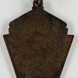 Reverse of shield shaped tarnished metal medal.