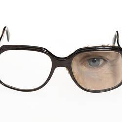 Plastic prosthetic glass blue/grey left eye with upper left cheek, eyebrow and eyelashes attached to brown plastic spectacles.