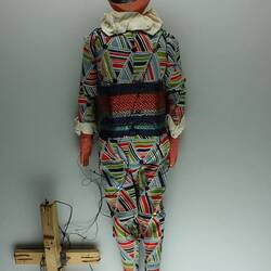 Back of male marionette, colourful costume, black hat. Wooden handle, strings attached.