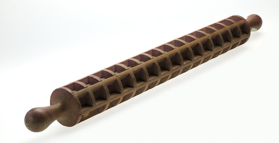 Wood cylindrical hand roller with squares all along & around surface to create pockets.