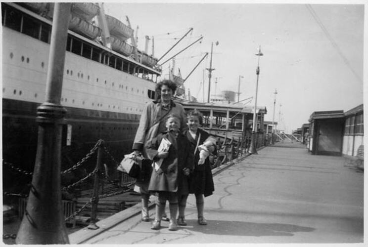 Woman and child stand on dock beside a large ship.