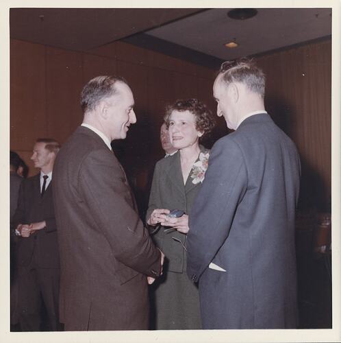 Woman holding gift talks to two men.