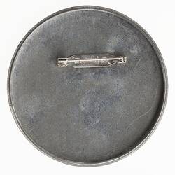 Back of round metal badge with metal pin and faint maker's details.