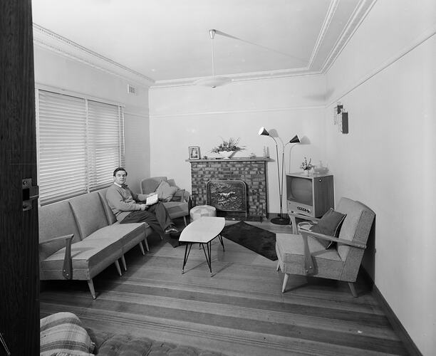 Man holding a book while sitting on a couch in a domestic living room.