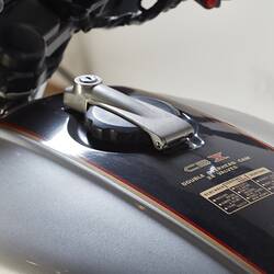 Silver motor cycle. Black tank detail, top view. Model type and safety in gold lettering.