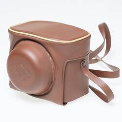 Light tan plastic camera carry case with shoulder strap.