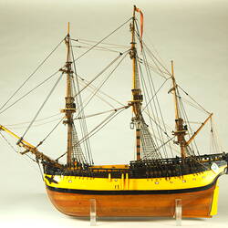 Model ship with wooden hull painted yellow and three masts, facing left.