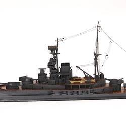 Wooden grey naval ship model with central tower, mast, mounted guns on wooden decks. Profile.