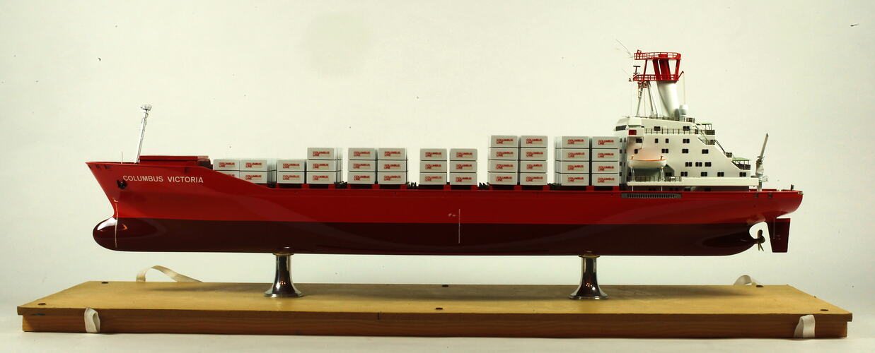 Container ship with red hull facing left.