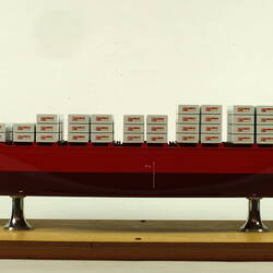 Container ship with red hull facing left.