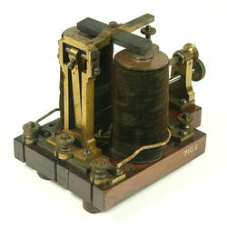 Brass apparatus with battery in centre on wooden base, three quarter view.