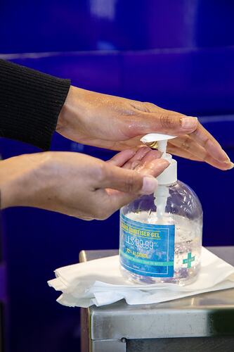 Hands using pump bottle of clear liquid hand sanitiser.