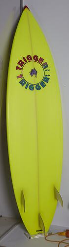 Yellow surfboard with circular logo. Three fins.