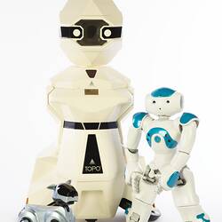 Cream plastic robot with angular human-like shape, ie. head, shoulders, waist and legs. Siver robot dog at left, smaller blue white root at right.