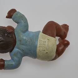 Baby doll wearing a blue top and white pants. The doll has dark brown skin and hair. Laying position.