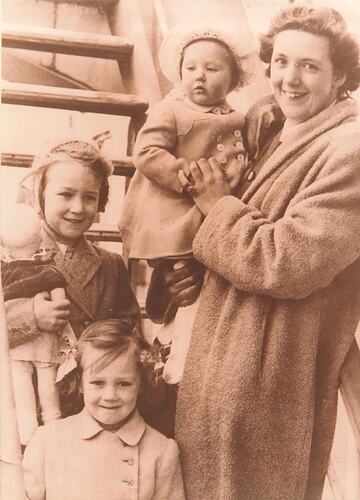 Three young girls with woman holding youngest one. They're in front of a ship's staircase.