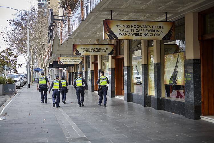 Five police officers walking along empty footpath outside closed theatre.