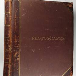Worn brown photograph album with gold letters and lines on spine.
