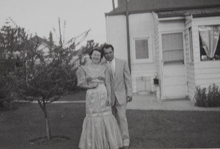 Woman and man smile and pose in the garden of a house.