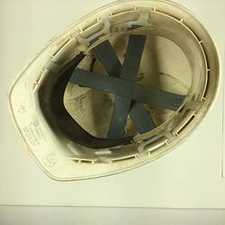 Internal view of used, scuffed white safety helmet. Grey webbing.