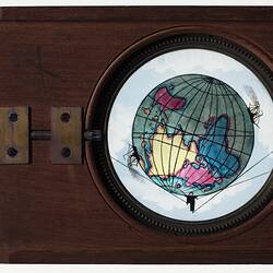 Back of wooden slide with handle on left side. Central round glass slide with coloured illustration of Earth.
