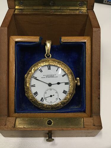 Ornate gold watch with white face housed in a wooden velvet-lined box.
