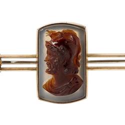 Gold bar brooch with centrally placed, rectangular cameo. Made of dark brown hardstone the cameo features a bearded male bust facing left with lighter brown background.