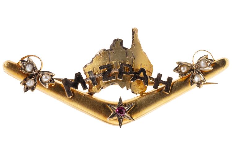 Back of gold boomerang with a map of Australia behind the words 'Mizpah'. Has seed pearls and a small ruby.