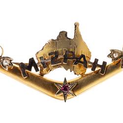 Back of gold boomerang with a map of Australia behind the words 'Mizpah'. Has seed pearls and a small ruby.