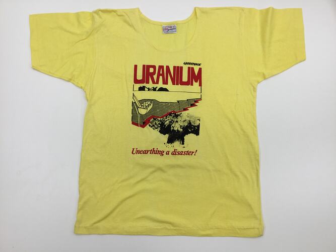 Yellow t-shirt with printed excavator bucket digging and mushroom cloud. Red text above and below.