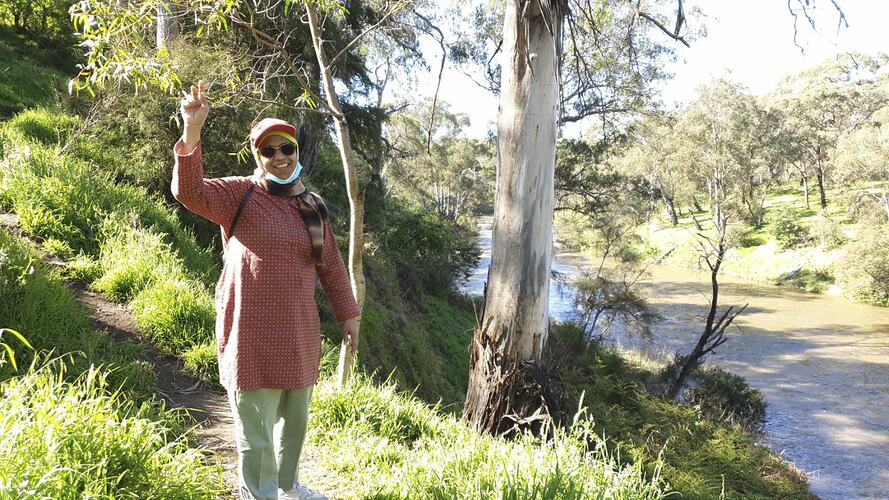 Woman posing in bushland beside a river.