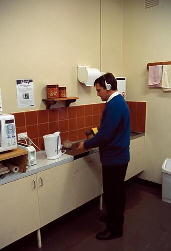 Michael Greenwood wearing remote transceiver headset, in kitchen. Melbourne Coastal Radio Station, Cape Schanck, Victoria
