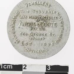 Round silver coloured medal with text.