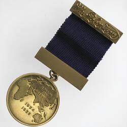 Round gilt medal with 2  bars and purple ribbon. Map of world, text around.