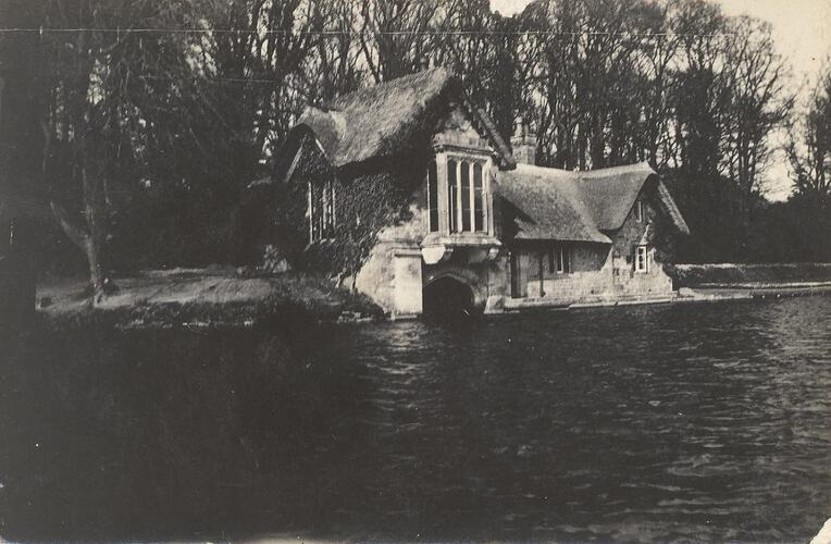 Thatched building by water with trees behind.