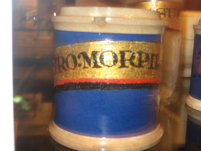 Ceramic jar with blue body. Gold painted label with black text.