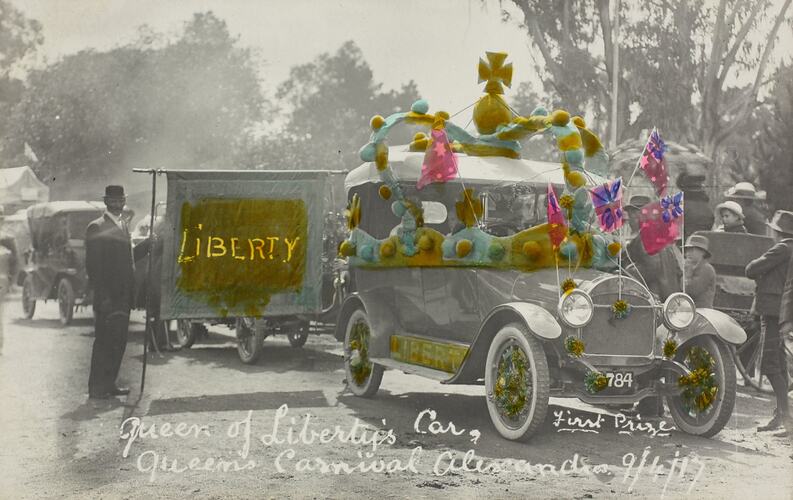 Car in street parade decorated with hand coloured Australian flags and crown in blue, pink, green and gold.