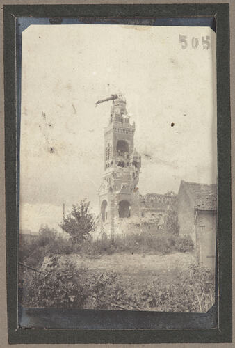 Bomb damaged stone building with tower and garden surrounding.