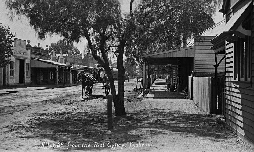 horse and cart in the middle of the tree-lined street. Shop verandas extend down both sides of the street.