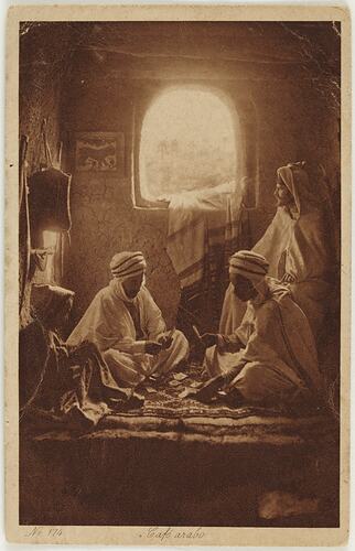 Men in headdresses and robes seated in front of arched window.