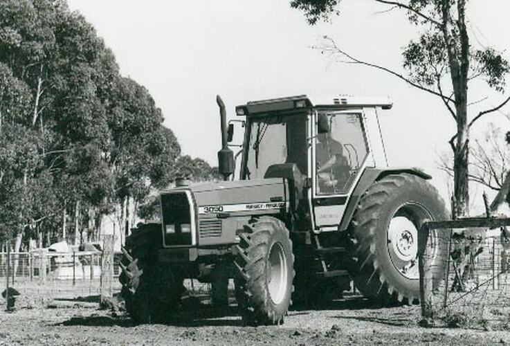 Man driving a tractor with disc plough attached through a farm gate.