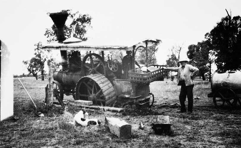 Bogged traction steam engine. Woman stands on it and a man leans against the back. Furphy water cart at right.