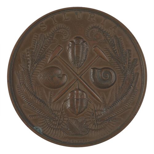 Medal with text, two crossed geological hammers, fossils and graptolites.