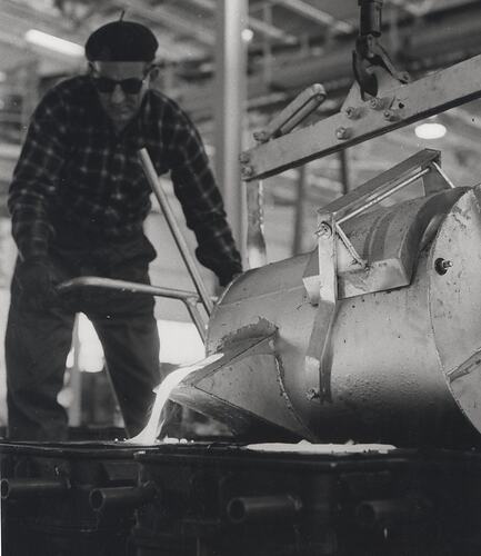 A man wearing dark glasses and a hat pouring molten metal into a mould.