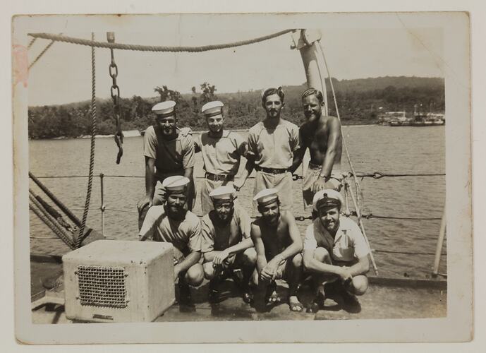 Eight seamen, four standing and four kneeling, on dock of ship
